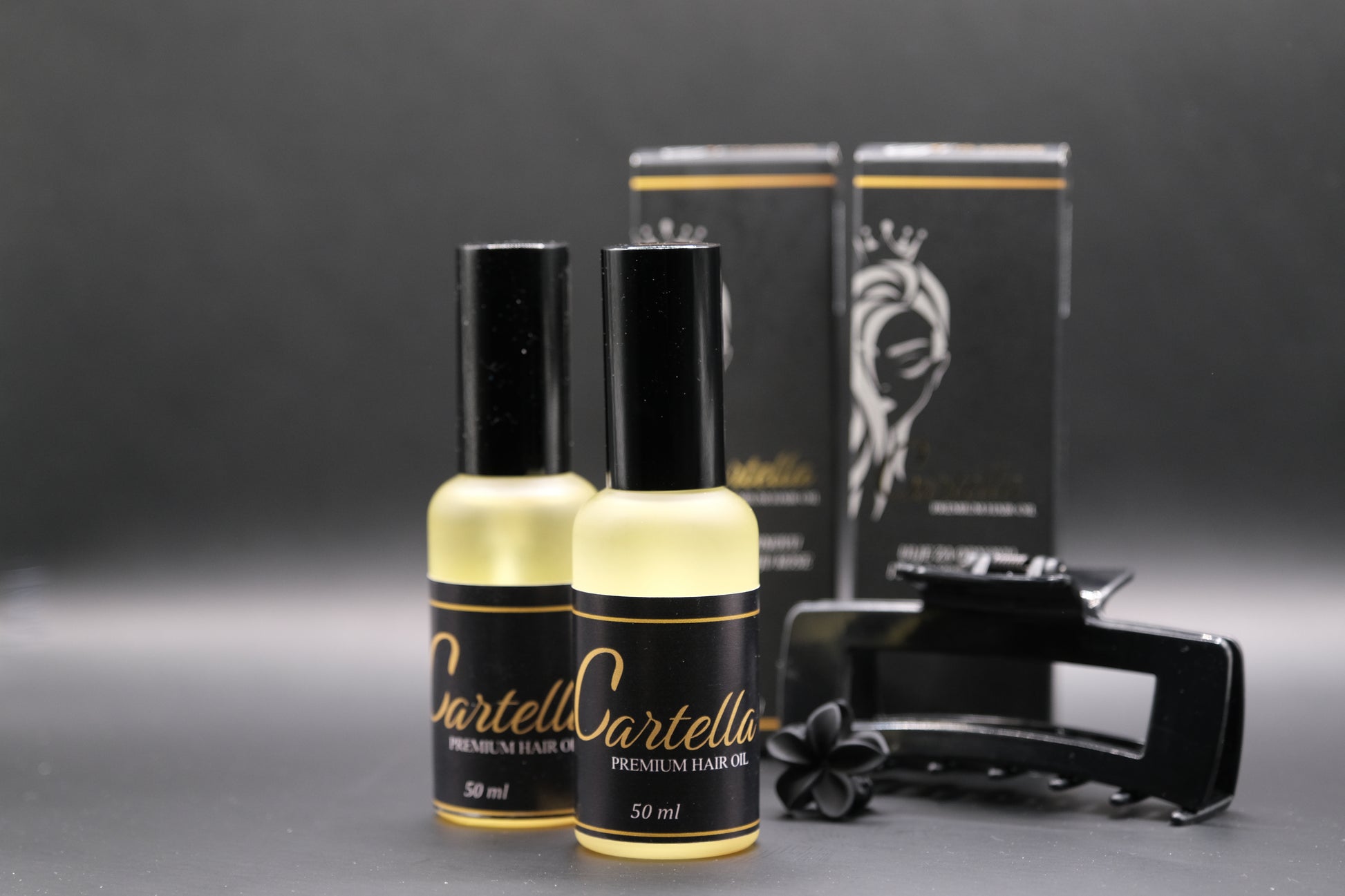 Two bottles of Cartell Cartella hair oil with a comb and packaging on a dark background
