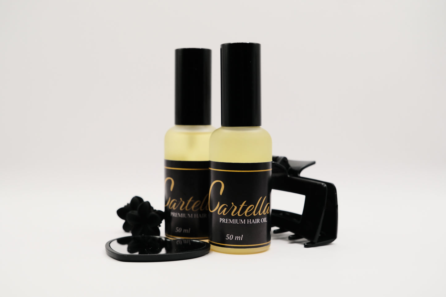 Two bottles of Cartella hair oil with a black cap on a white background