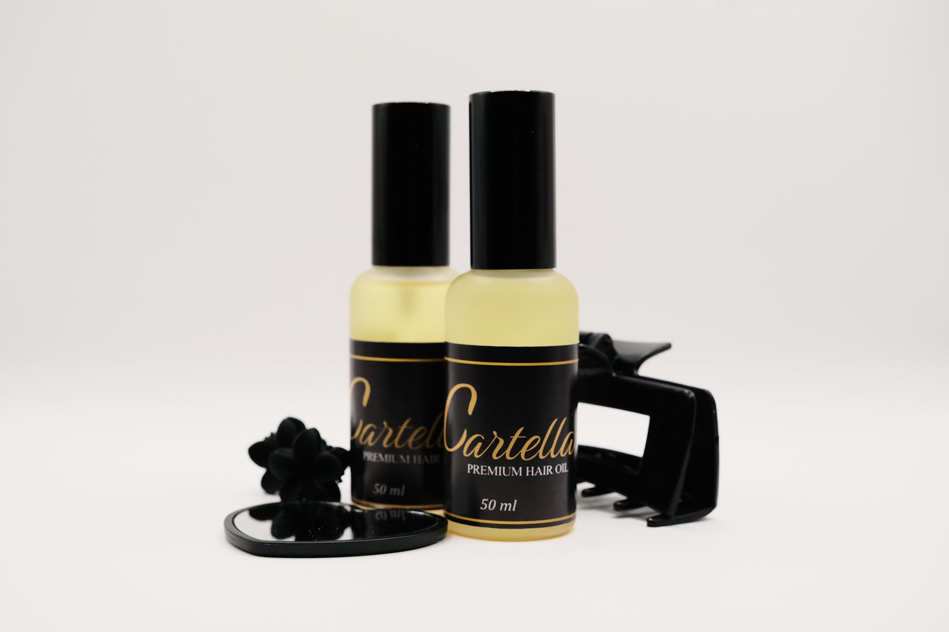 Two bottles of Cartella hair oil with a black cap on a white background