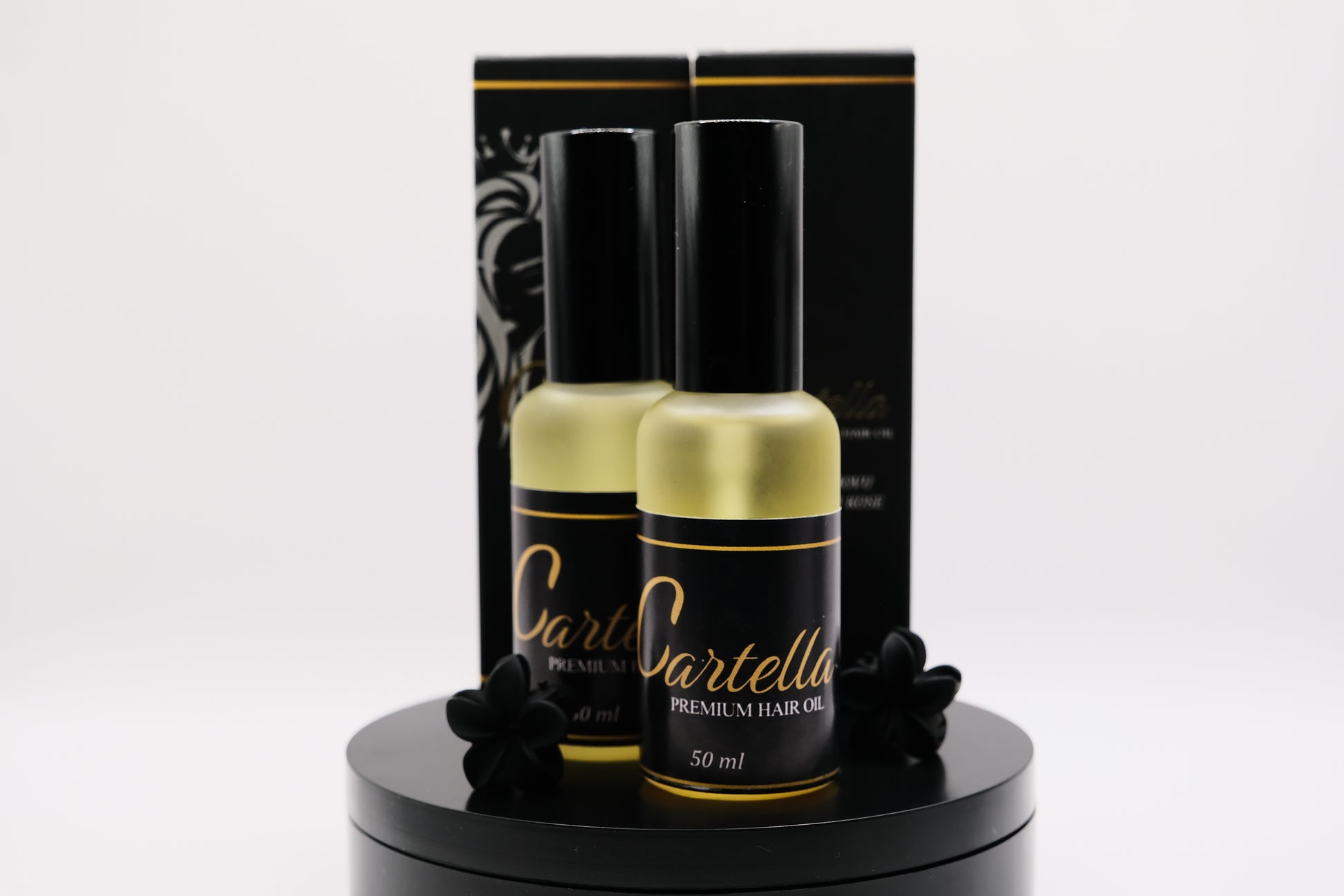 Two bottles of Dartella hair oil on a black stand with a black box in the background.