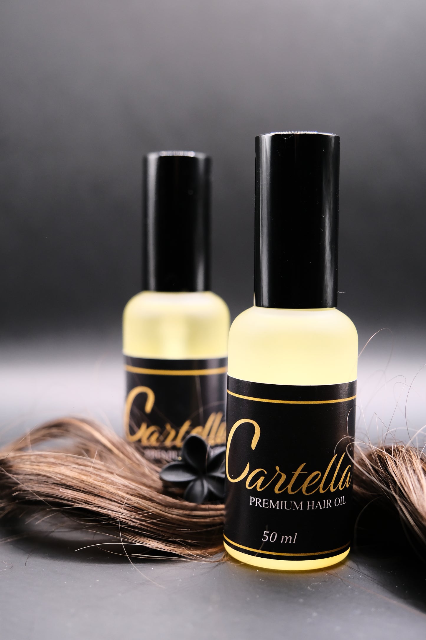 Two bottles of Cartella hair product on a dark background